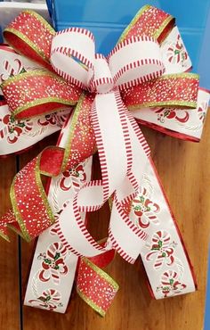 a red and white christmas bow with apples on it sitting on top of a wooden table