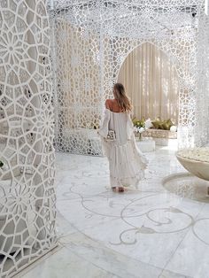 a woman in white dress walking through an intricately designed room with large circular sculptures