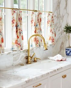 a kitchen with marble counter tops and gold faucet, white cabinets and windows