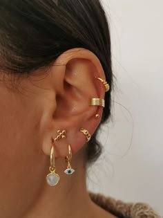 a close up of a person wearing gold ear cuffs and piercings on their ears