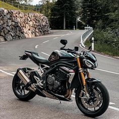 a black motorcycle parked on the side of a road next to a stone wall and trees