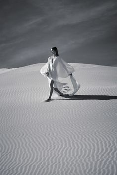 black and white photograph of woman walking in the desert with her coat over her shoulders