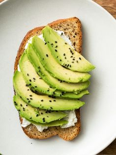 an open face sandwich with avocado and cottage cheese on it sitting on a white plate