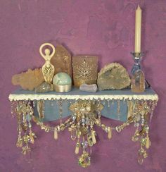 a wall shelf with candles, rocks and other items on it against a purple wall