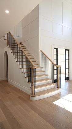 a white staircase with black railing and wood flooring in an empty room next to a doorway