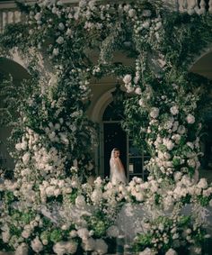 a bride standing in the doorway of a building surrounded by white flowers and greenery