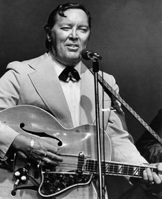 a man in a suit and tie holding a guitar while standing next to a microphone