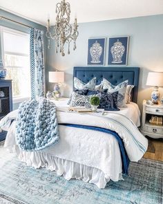 a blue and white bedroom with chandelier, bed, rugs and pillows