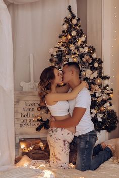 a young man and woman are kissing in front of a christmas tree with lights on it