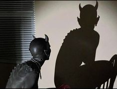 the shadow of a demon sitting in a chair next to a man with horns on his head