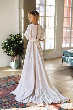 a woman in a white wedding dress standing on a rug with her back to the camera