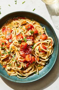 a plate of pasta with tomatoes, parmesan cheese and herbs on the side