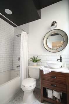 a white toilet sitting next to a bath tub under a bathroom mirror on top of a wooden cabinet