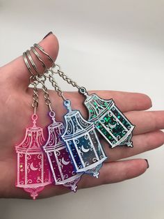 a hand holding three different colored key chains in it's left hand, one with a birdcage and the other with a clock