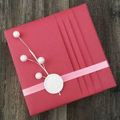 a red gift box wrapped in pink paper with white ribbon and pom - poms