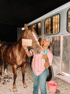 a woman standing next to a brown horse in front of a trailer with its door open