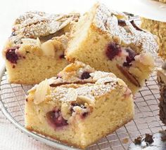 several pieces of cake sitting on top of a cooling rack with powdered sugar and fruit toppings