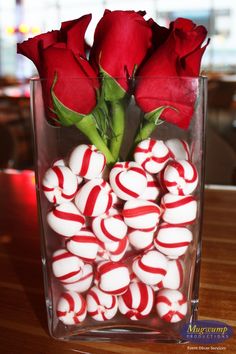 red roses and white candy canes in a clear vase on a wooden table top