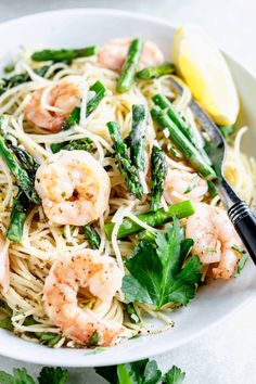 a white bowl filled with pasta and asparagus next to lemon wedged parsley