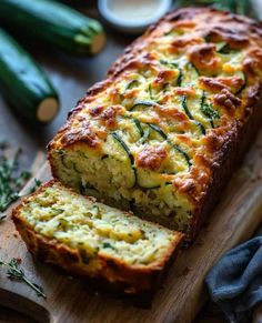 a loaf of zucchini bread sitting on top of a wooden cutting board next to green vegetables