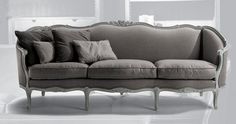 a couch with many pillows on it in a room that has white walls and flooring