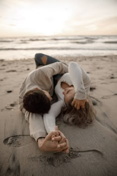 two people are laying on the sand at the beach with their hands in each other's pockets