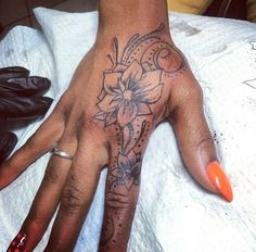 a woman's hand with a flower tattoo on it and an orange manicure