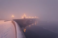 a bridge that is next to the water with snow on it and street lights in the distance