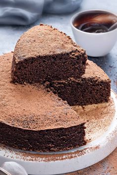 a chocolate cake on a white plate with powdered sugar and coffee in the background