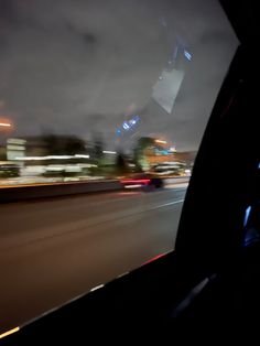 the view from inside a car at night with blurry lights and buildings in the background