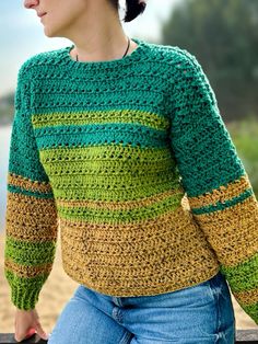 a woman wearing a green, yellow and brown crochet sweater standing on the beach