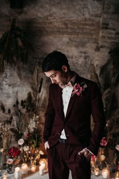 a man in a red suit and white shirt standing next to candles with his hands on his hips