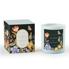 a candle that is next to a box on a white surface with flowers and butterflies around it