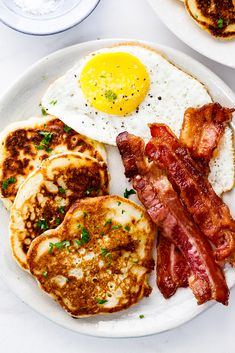 a plate with pancakes, eggs and bacon on it sitting next to another plate full of pancakes