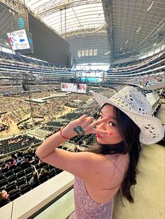 a woman wearing a hat standing in front of a crowd at a sporting event with her hand up to her face