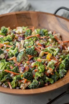 a wooden bowl filled with broccoli, carrots and other vegetables on top of a table