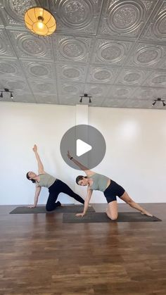 two people are doing yoga in an empty room with wood flooring and ceiling lights