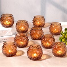 a bunch of glass candles sitting on top of a table next to grapes and a book