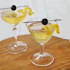 two martinis with lemon and olive garnishes on a wooden table top