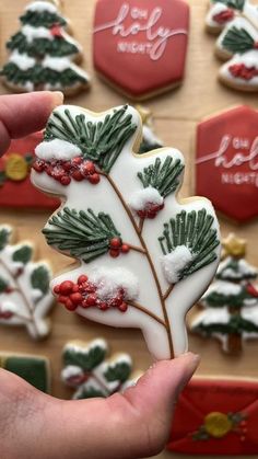 a hand holding a decorated christmas tree cookie in front of some cookies on a table