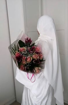 a woman wearing a white veil holding a bouquet of flowers in her hands and looking at the door