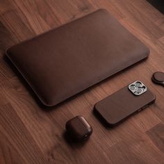 a brown leather case sitting on top of a wooden table next to an iphone and earbuds