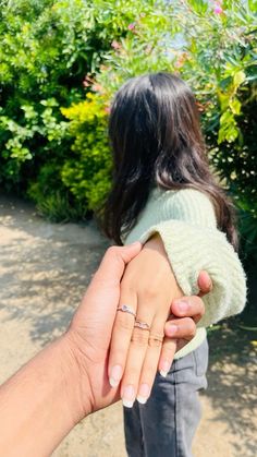 a woman holding the hand of a man in front of some bushes and flowers,