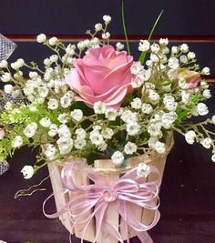 a pink rose in a basket with white flowers and baby's breath on the side