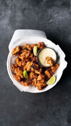 a white plate topped with fried food next to a small bowl of ranch dressing and lime wedges