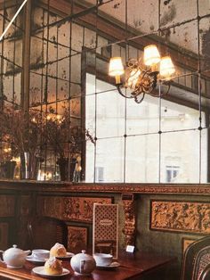 a dining table with tea cups and plates on it in front of a large window