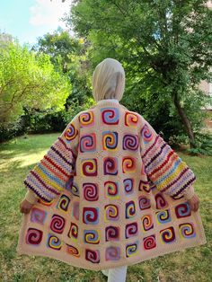 a woman standing in the grass wearing a colorful crochet blanket