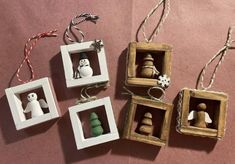 four small wooden ornaments are hanging from twine strings on a pink surface with snowmen