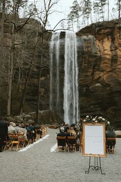 an outdoor ceremony with a waterfall in the background and people sitting at tables under it