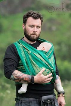 a man holding a baby wrapped in a green wrap